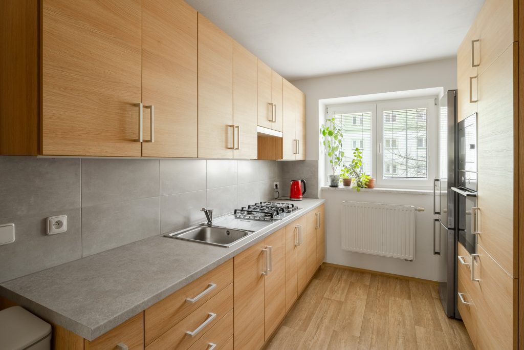 Moderní minimalistická kuchyně - pohled směrem k oknu, vestavěné spotřebiče (mikrovlnka, trouba, sporák), šedá stylová kuchyňská linka.